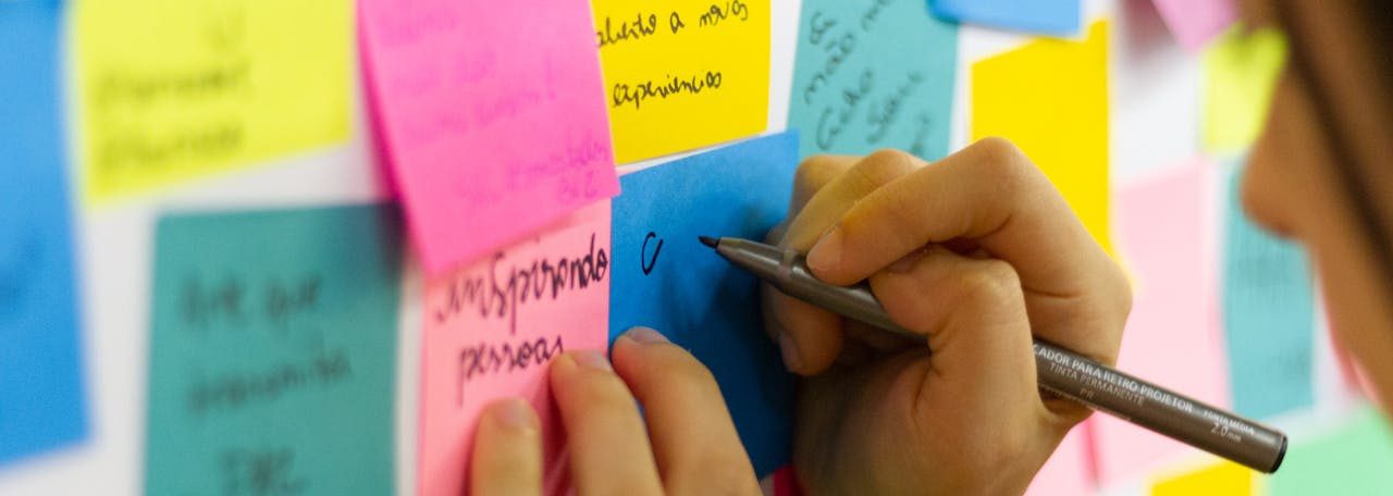 Person Writing on Pink Sticky Notes